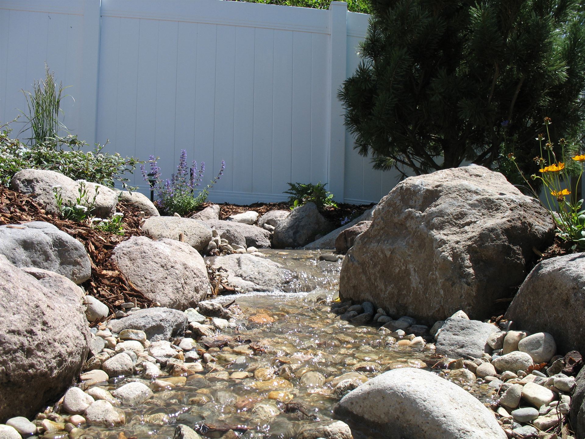 Running stream feature bordered by large boulders and ornamental grasses