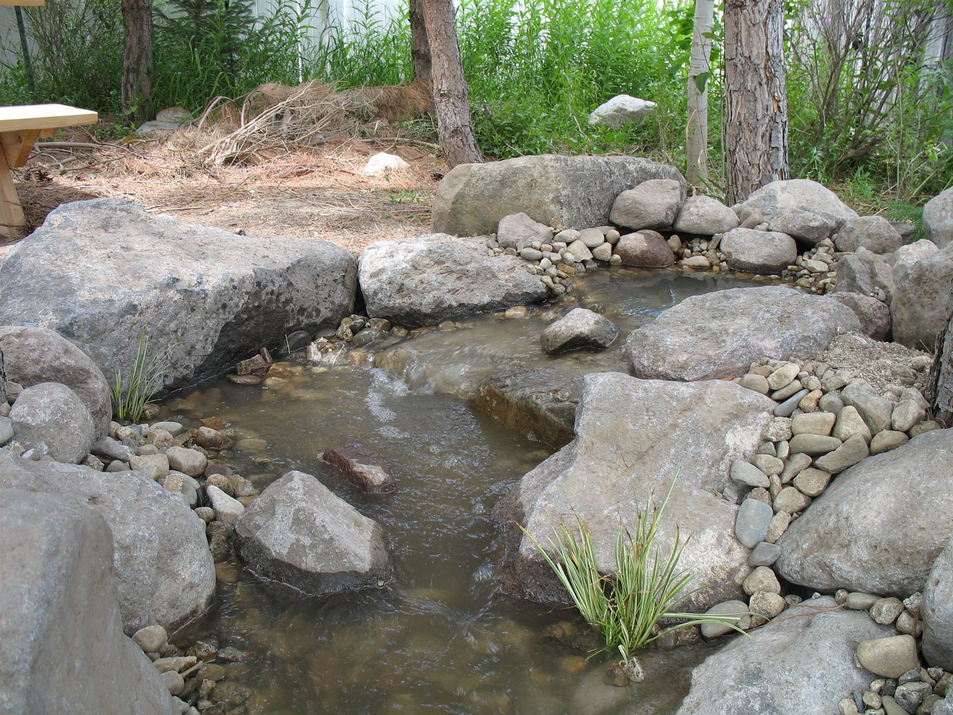 A white footbridge crossing a boulder-lined pond in a Botanical Zen landscape design