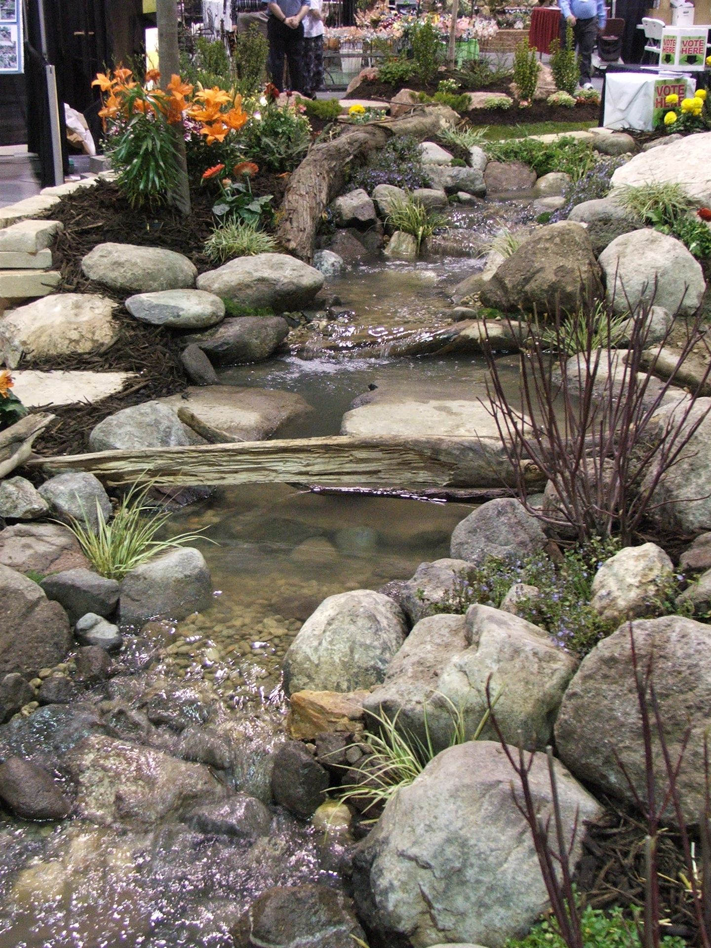 Completed show-garden water feature with stepping stones and flowers in bloom